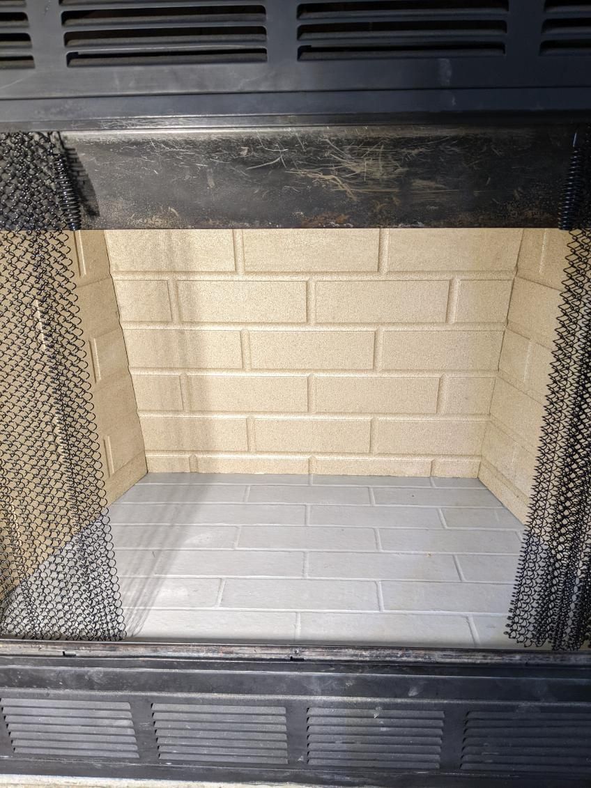 Empty fireplace with gray floor, beige brick walls, and black trim.