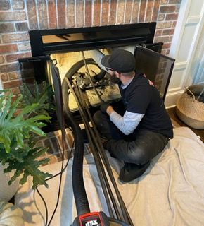 A person cleaning a fireplace with tools. Brick surround, black door, tools are silver.
