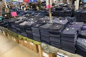 Stacks of folded dark pants displayed on tables in a clothing store or market.