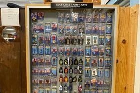 Gulf Coast Army display case filled with many small souvenir items and pins behind glass