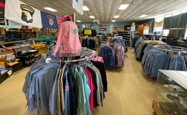 Clothing store interior with racks of shirts and jackets, including a pink hoodie display in the center.