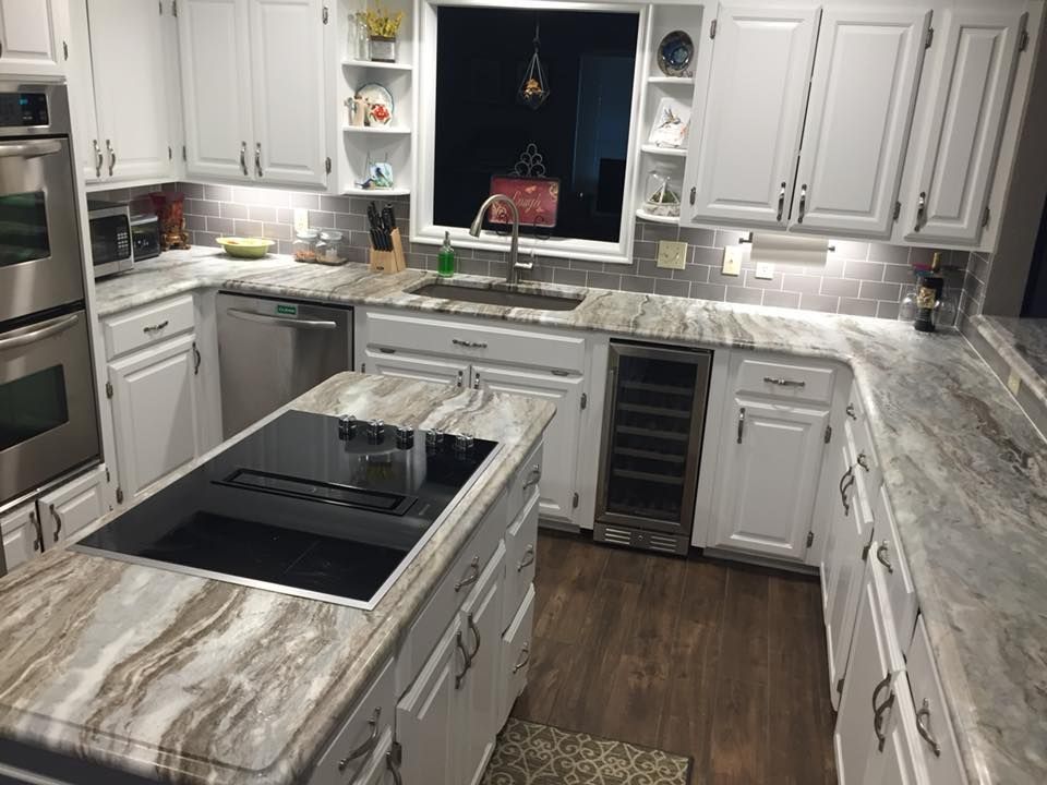 A kitchen with white cabinets , granite counter tops , stainless steel appliances and a large island.