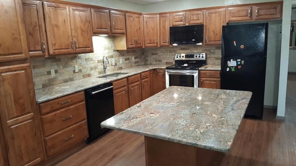 A kitchen with wooden cabinets , granite counter tops , and a black refrigerator.