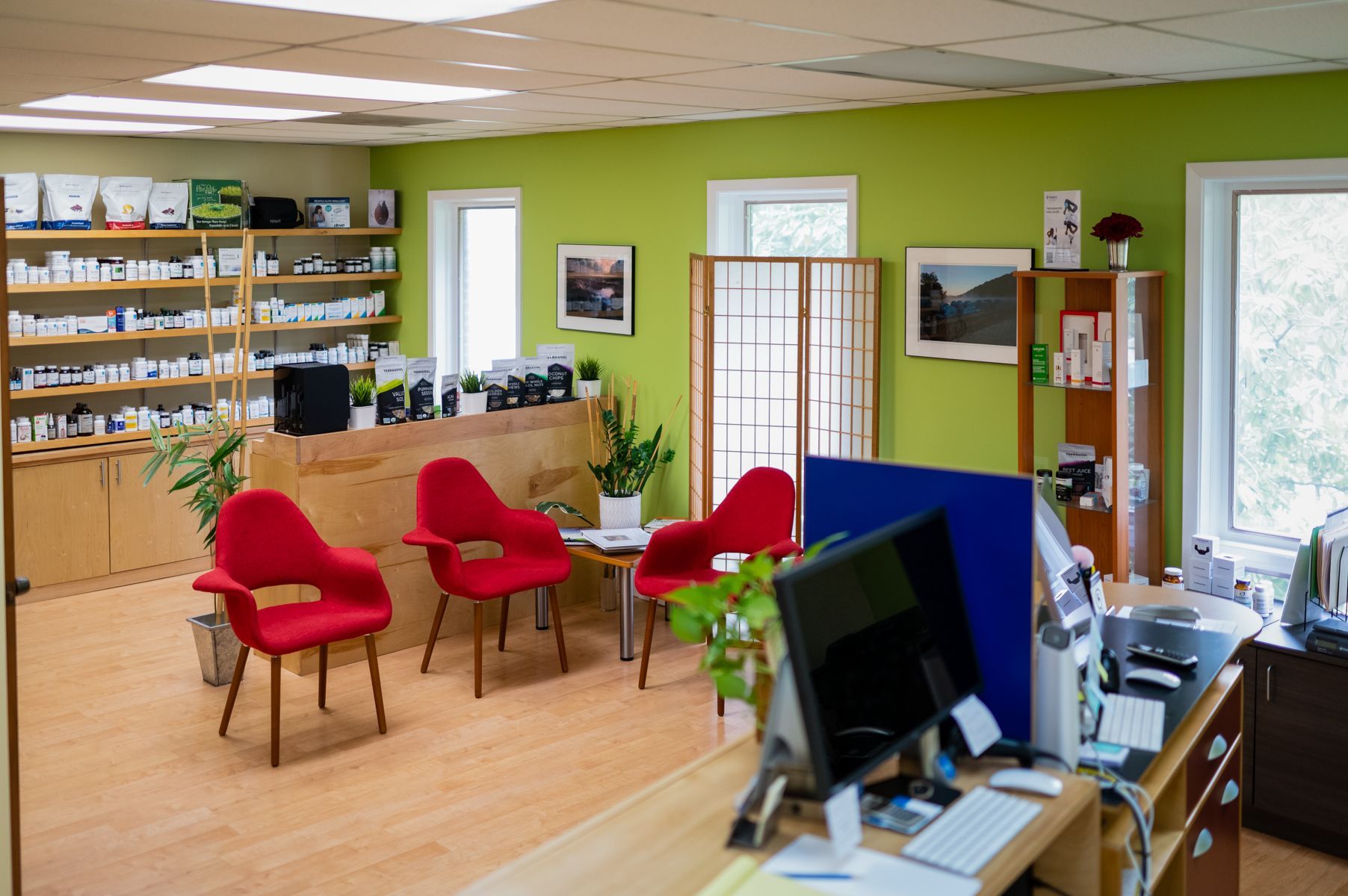 Reception area with red chairs, green wall, and wooden shelves stocked with products.