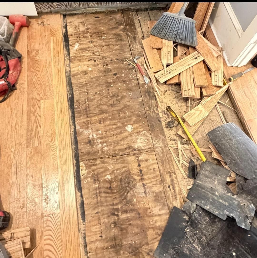 Partially removed wooden floor with tools and debris in a room under renovation