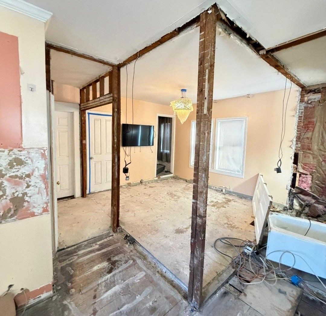 Partially demolished room with exposed wood framing, debris, and a wall-mounted TV in the background