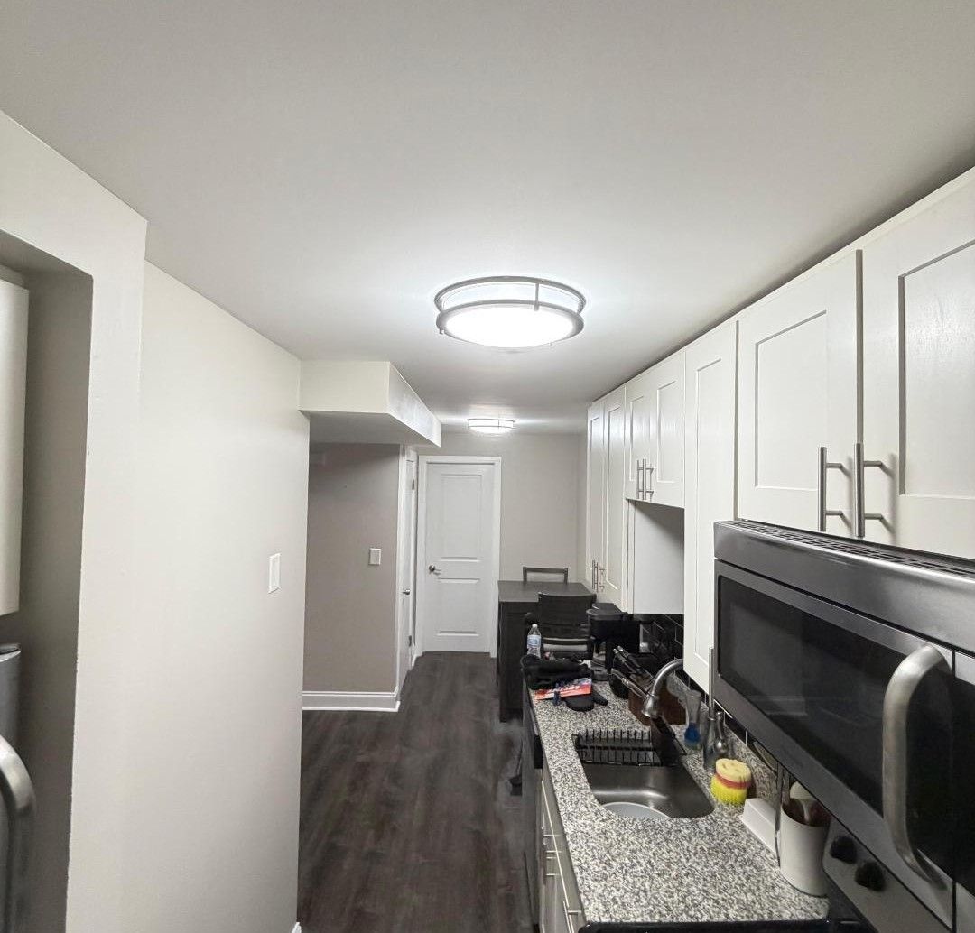 Modern kitchen with white cabinets, granite counter, dark floor, and stainless steel appliances.