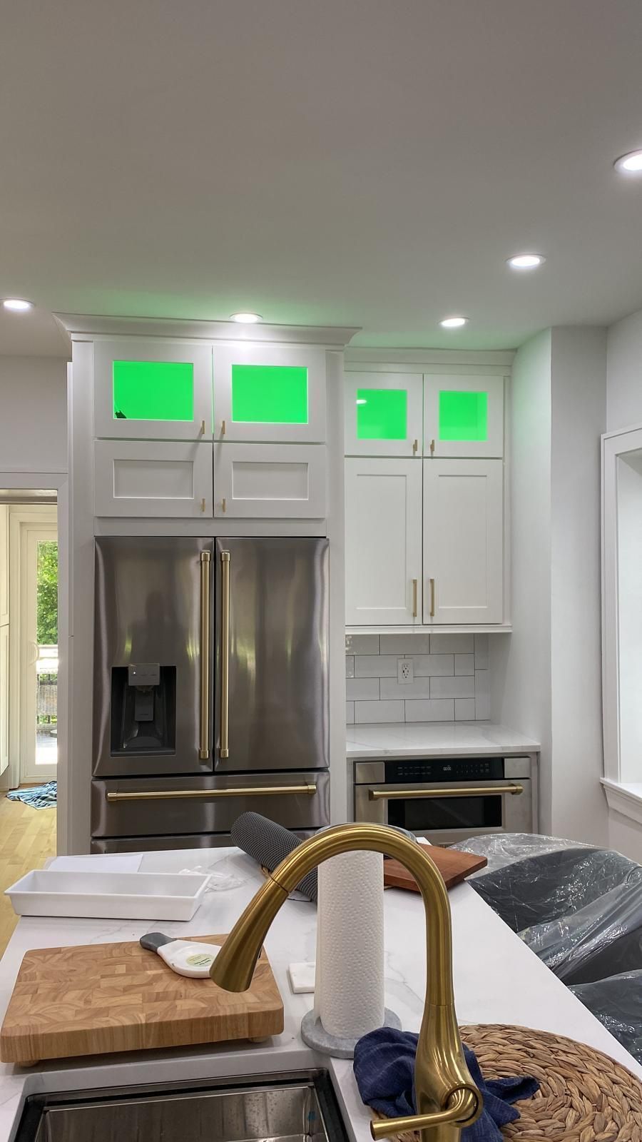 Modern white kitchen with stainless steel fridge, oven, and island faucet in foreground