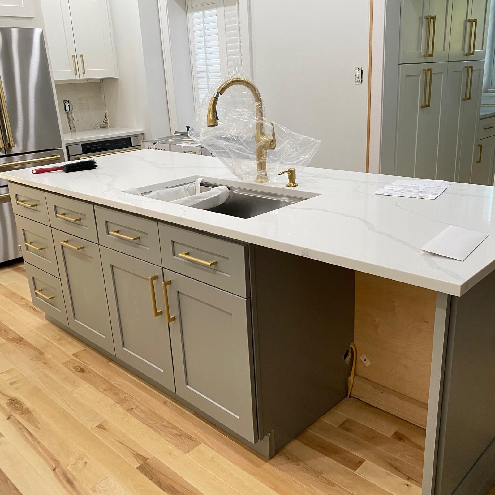 Modern kitchen island with white countertop, gray cabinets, brass pulls, and a farmhouse sink
