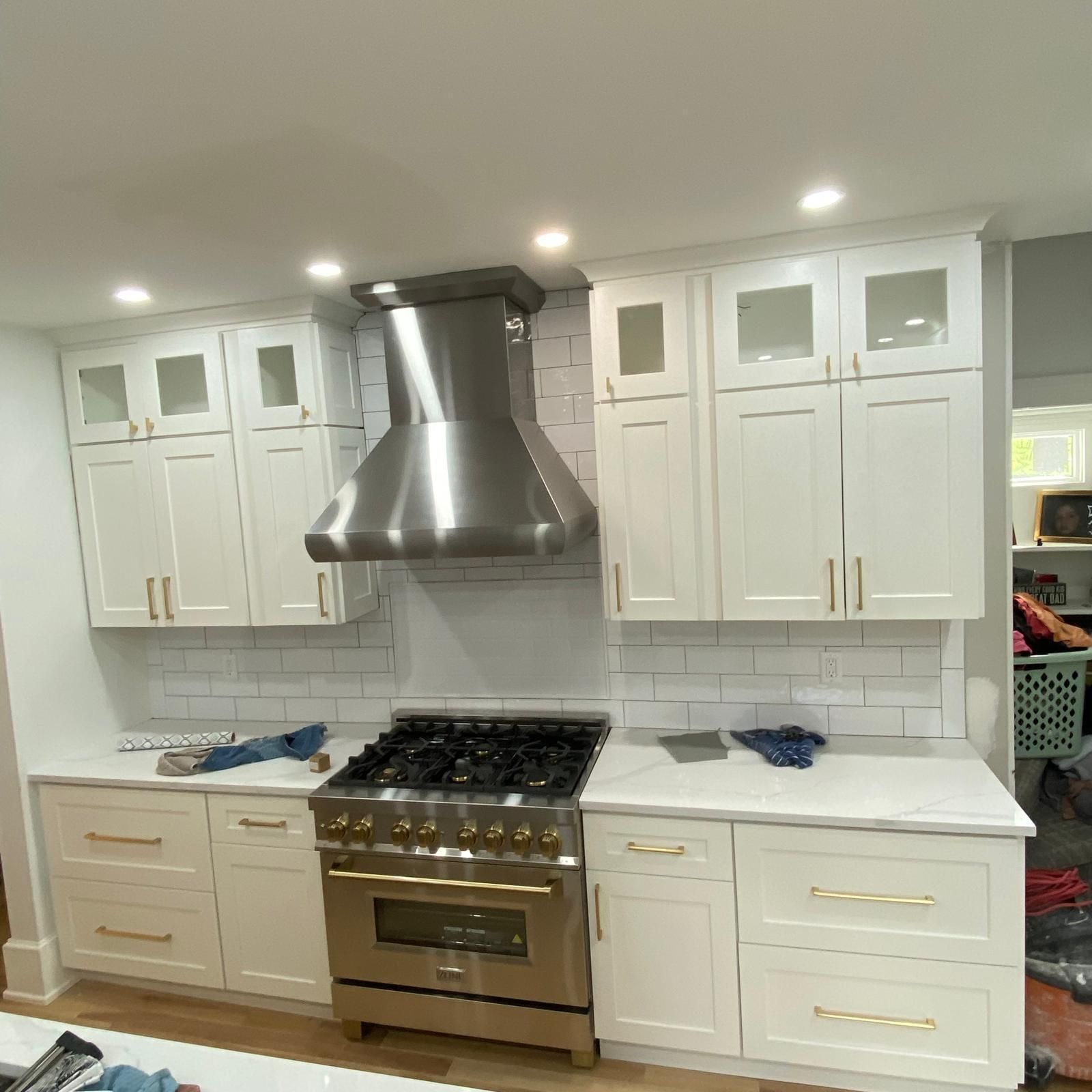 Bright white kitchen with stainless steel stove and hood, white cabinets, and marble-look countertops.