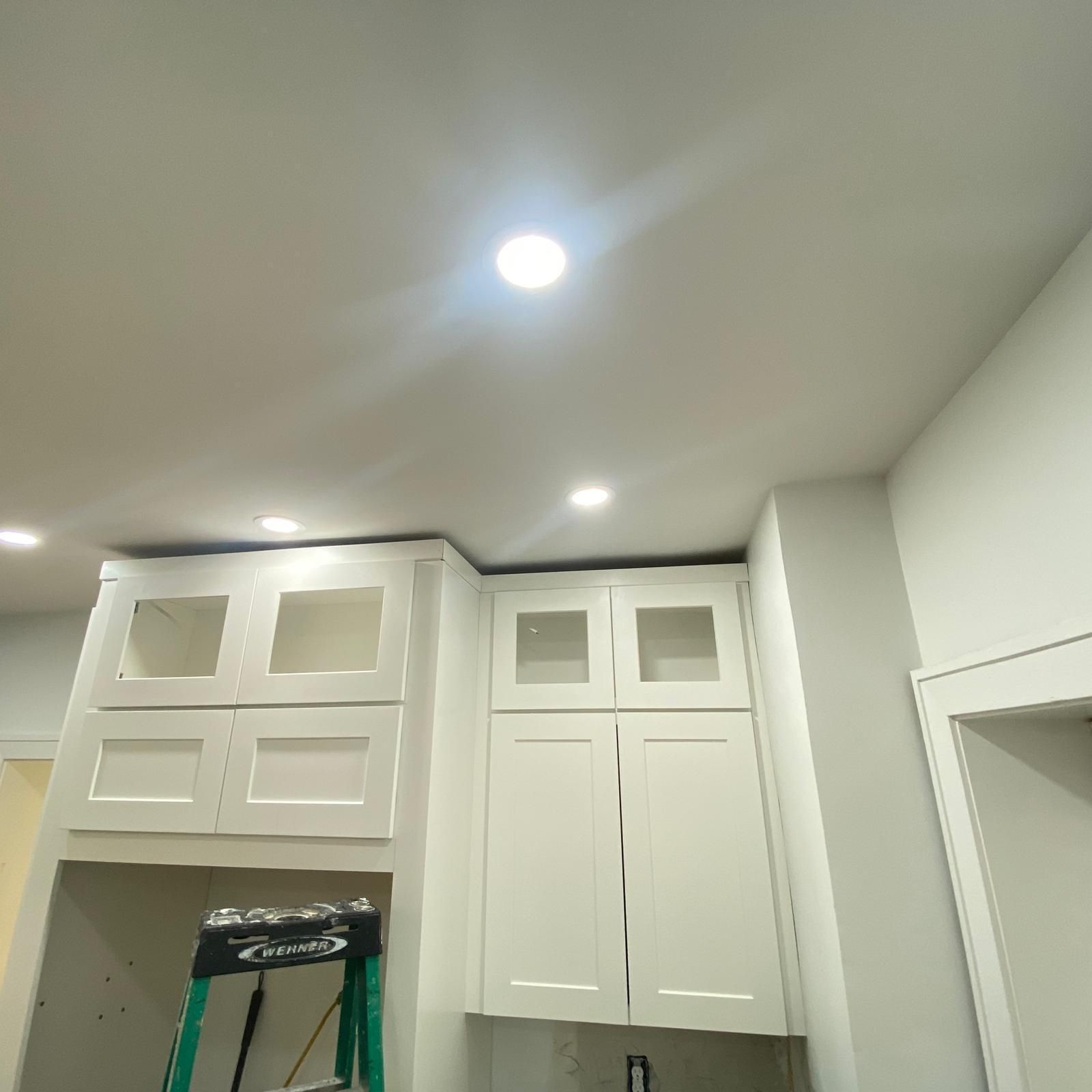 White cabinets and recessed ceiling lights in a kitchen under renovation, with a ladder below.
