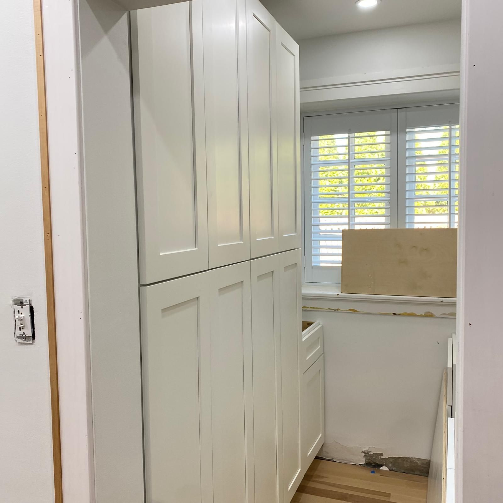 Narrow pantry with white cabinets and a window, partly under renovation with exposed floor area
