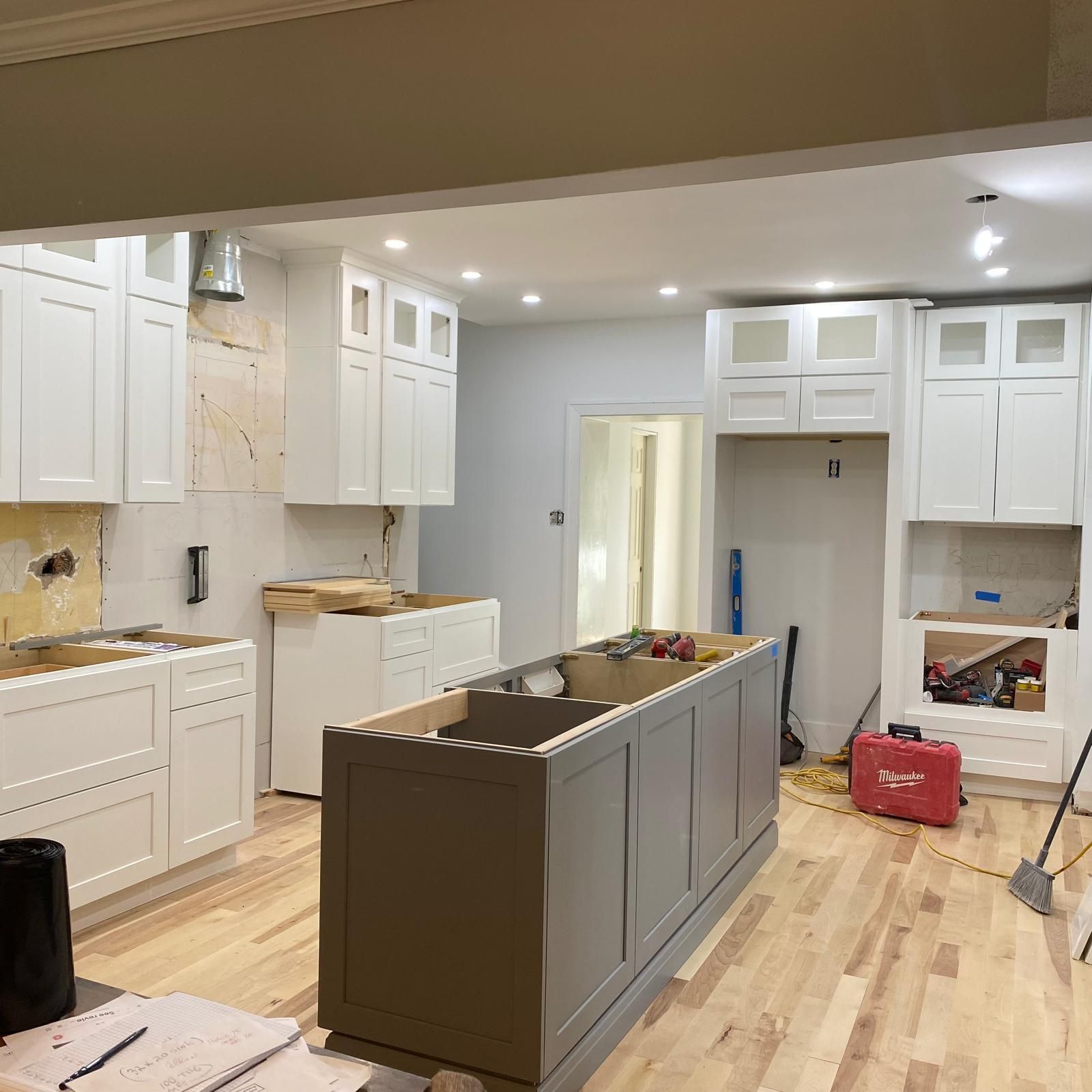 Kitchen renovation in progress with white cabinets, gray island, and unfinished flooring￼