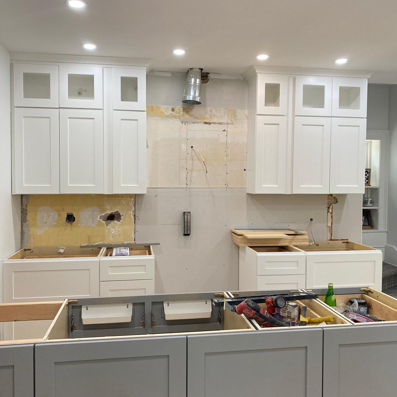 Kitchen under renovation with white cabinets, unfinished backsplash, and tools on a countertop