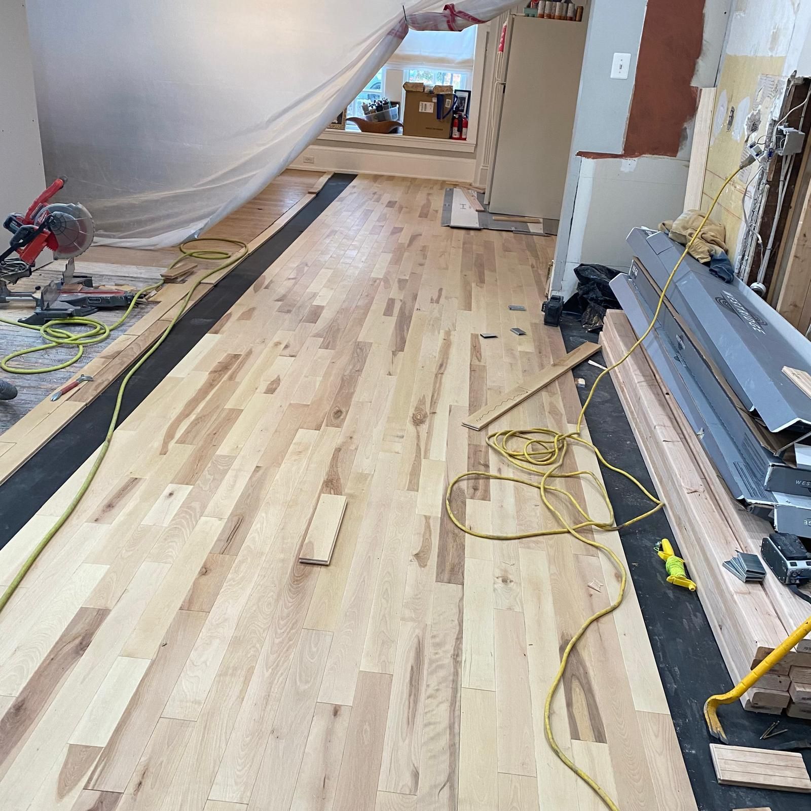 Wood floor installation in a renovation room with tools, cables, and covered furniture.