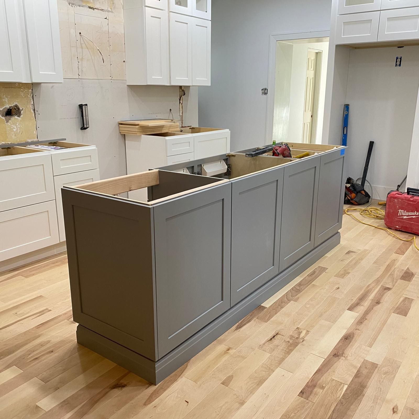 Gray kitchen island cabinet in an unfinished kitchen with white cabinets and wood flooring