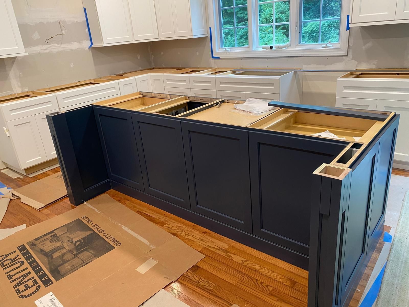 Kitchen under renovation with dark blue island cabinets and unfinished countertop in a bright room