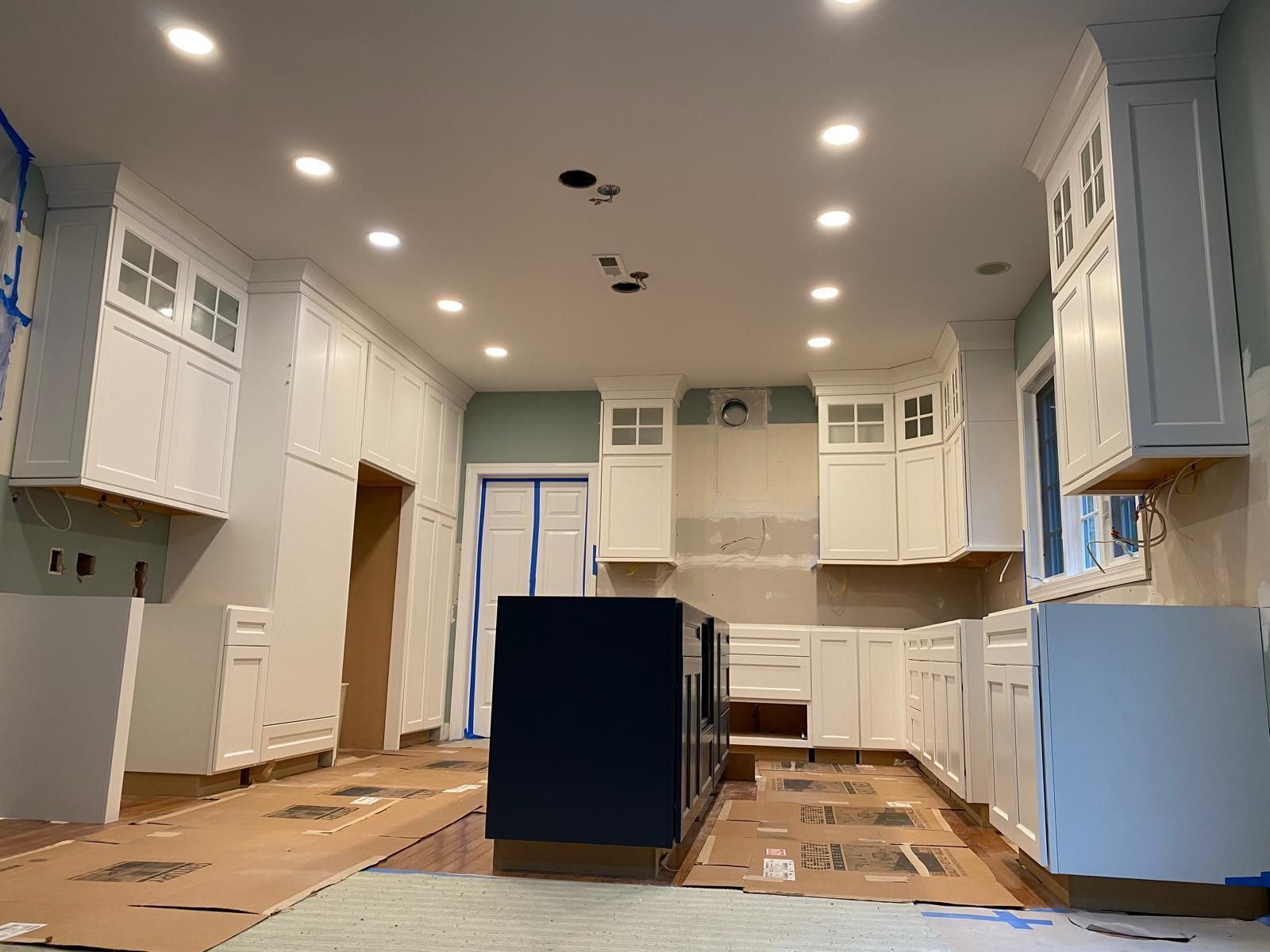 Bright kitchen under renovation with white cabinets, recessed lights, and an island wrapped in protective covering