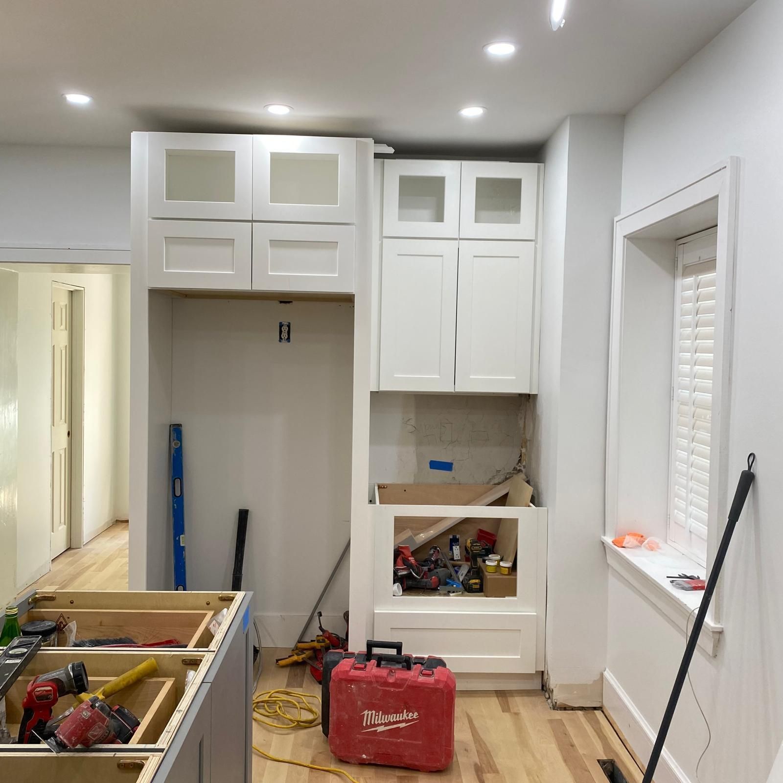 Kitchen under renovation with white cabinets, tools, and construction materials scattered on the floor.