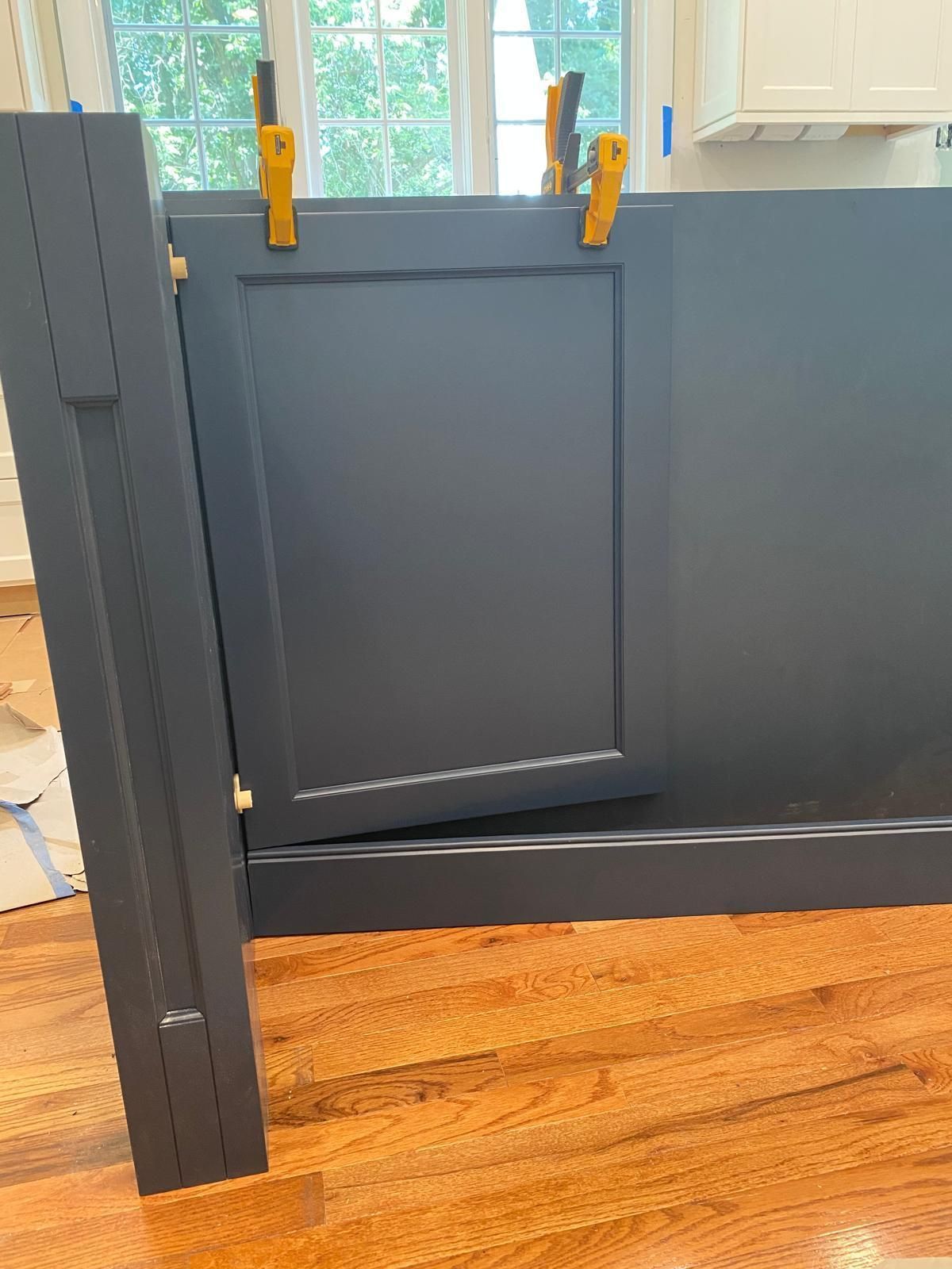 Gray half door with yellow clamps in front of a bright window, inside a room with wood floors