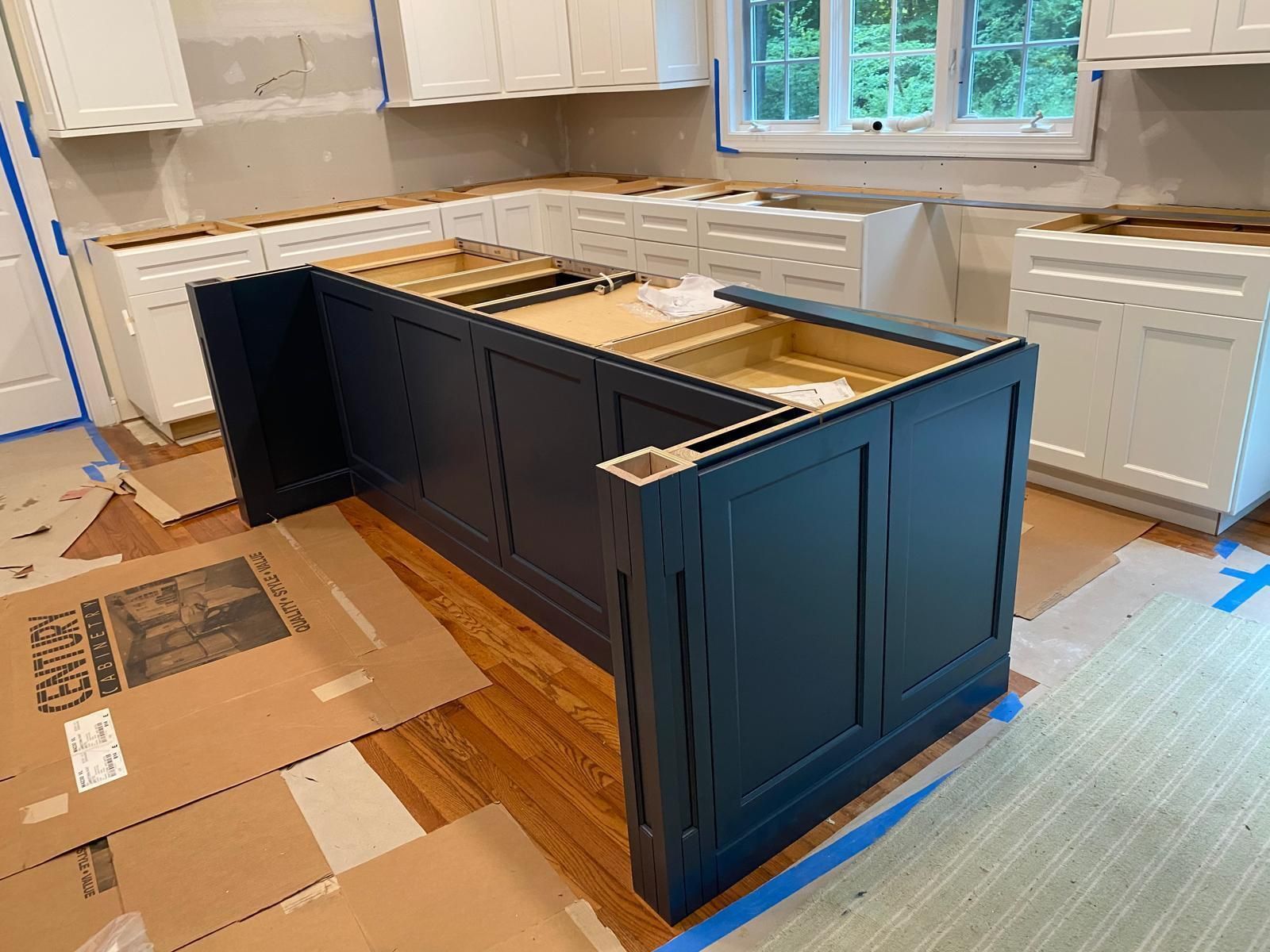 Kitchen renovation with dark navy island cabinets and unfinished countertops on a protected floor