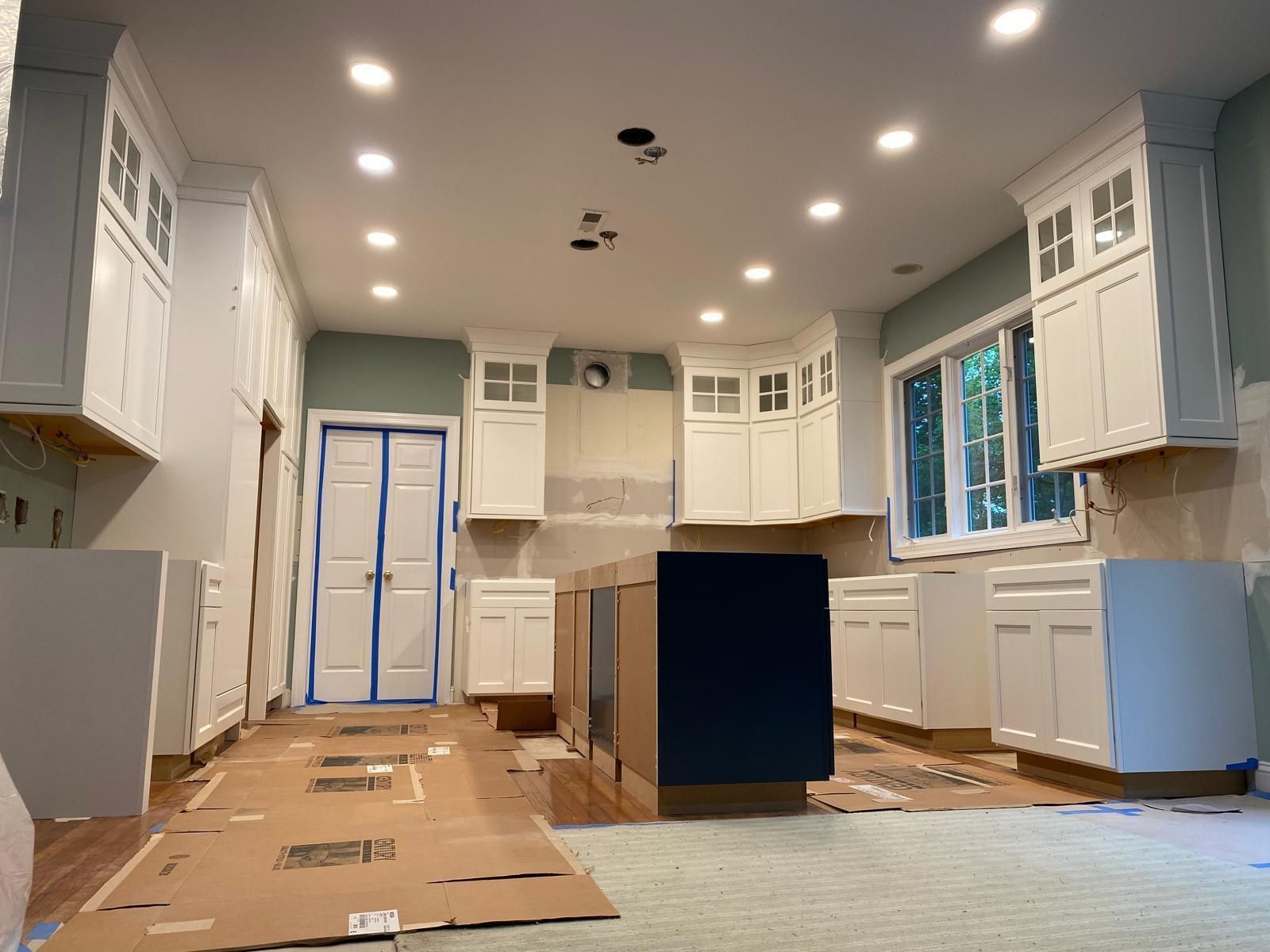Bright white kitchen under renovation with blue-taped cabinets, island, and cardboard on the floor