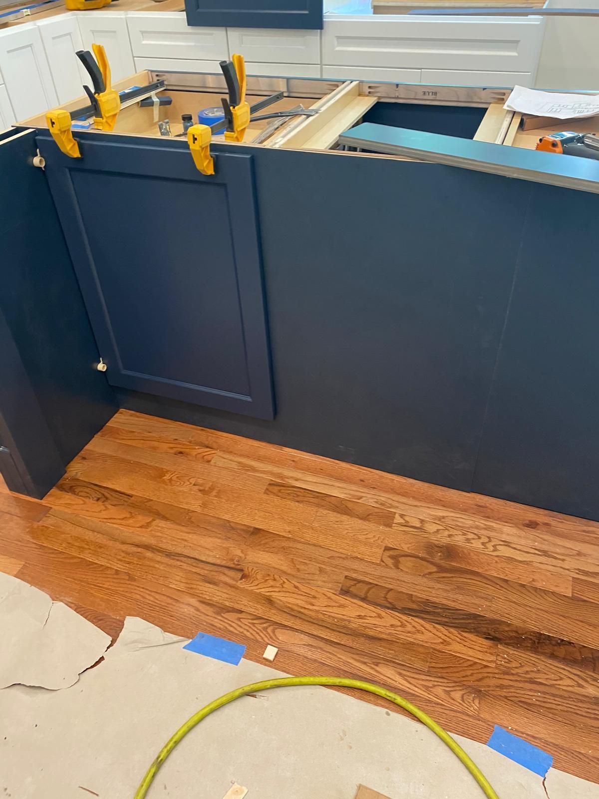 Blue kitchen cabinets with a wooden countertop, yellow tools on top, and cardboard covering the floor during renovation