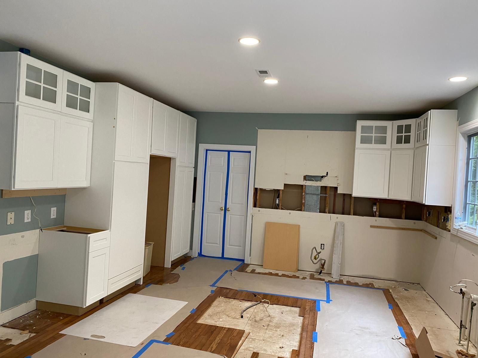 Unfinished kitchen with white cabinets, blue tape on floors, and brown tile backsplash under construction