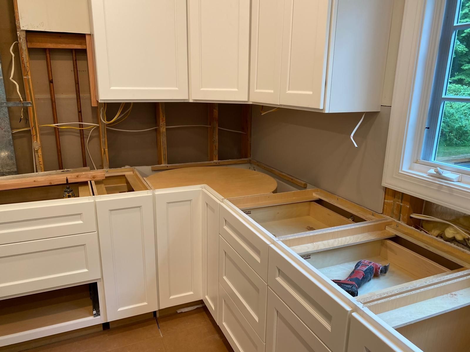 Kitchen under renovation with white cabinets, exposed wall studs, and partially removed countertops