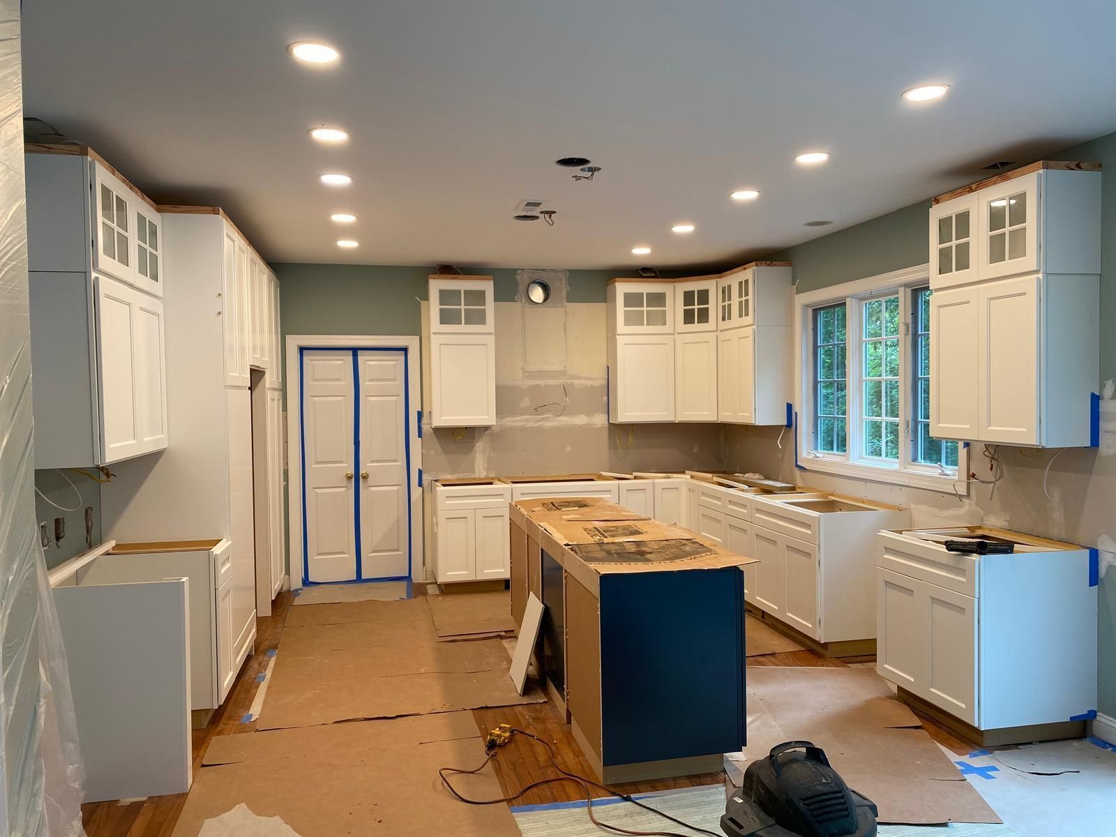 Renovated kitchen with white cabinets, blue island, and protective floor covering during construction.