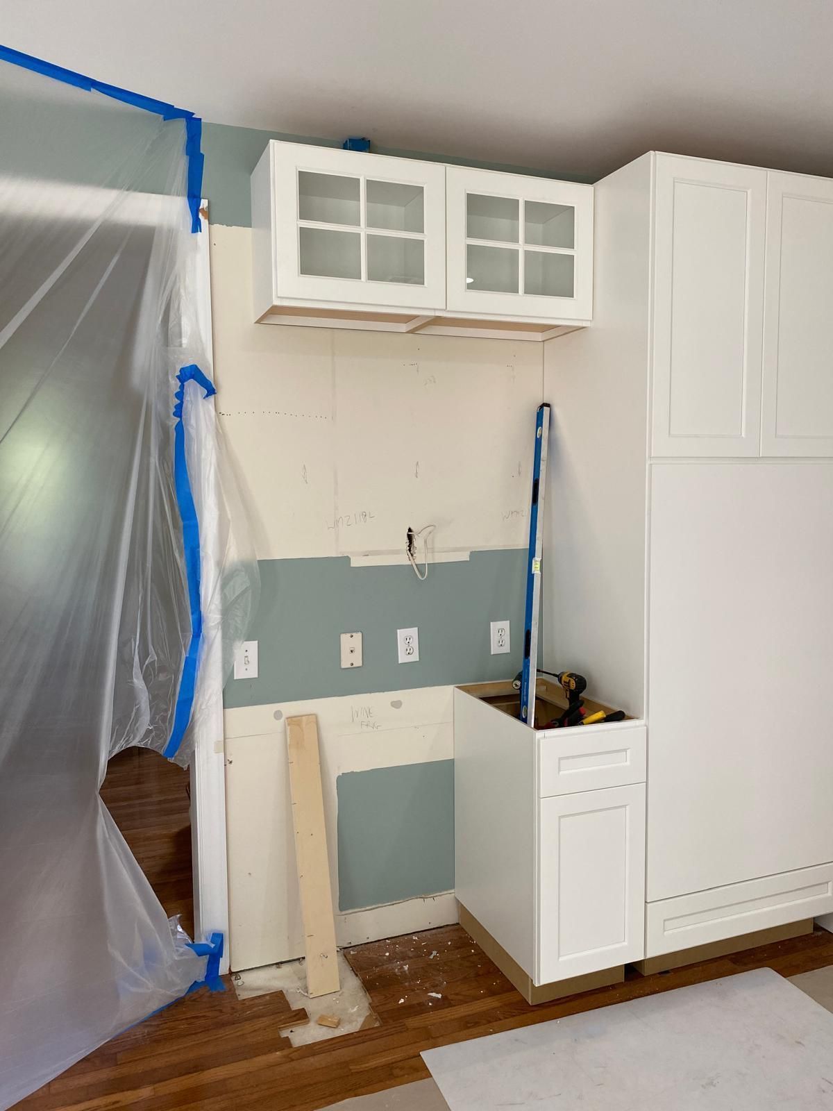 Partially renovated kitchen with white cabinets, blue-gray backsplash, and plastic-covered opening