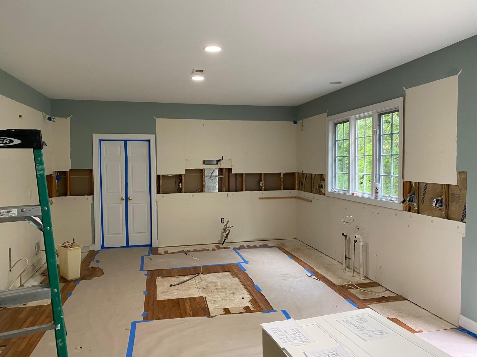 Unfinished kitchen remodel with white cabinets, blue tape, exposed floor, and open wall cabinets.
