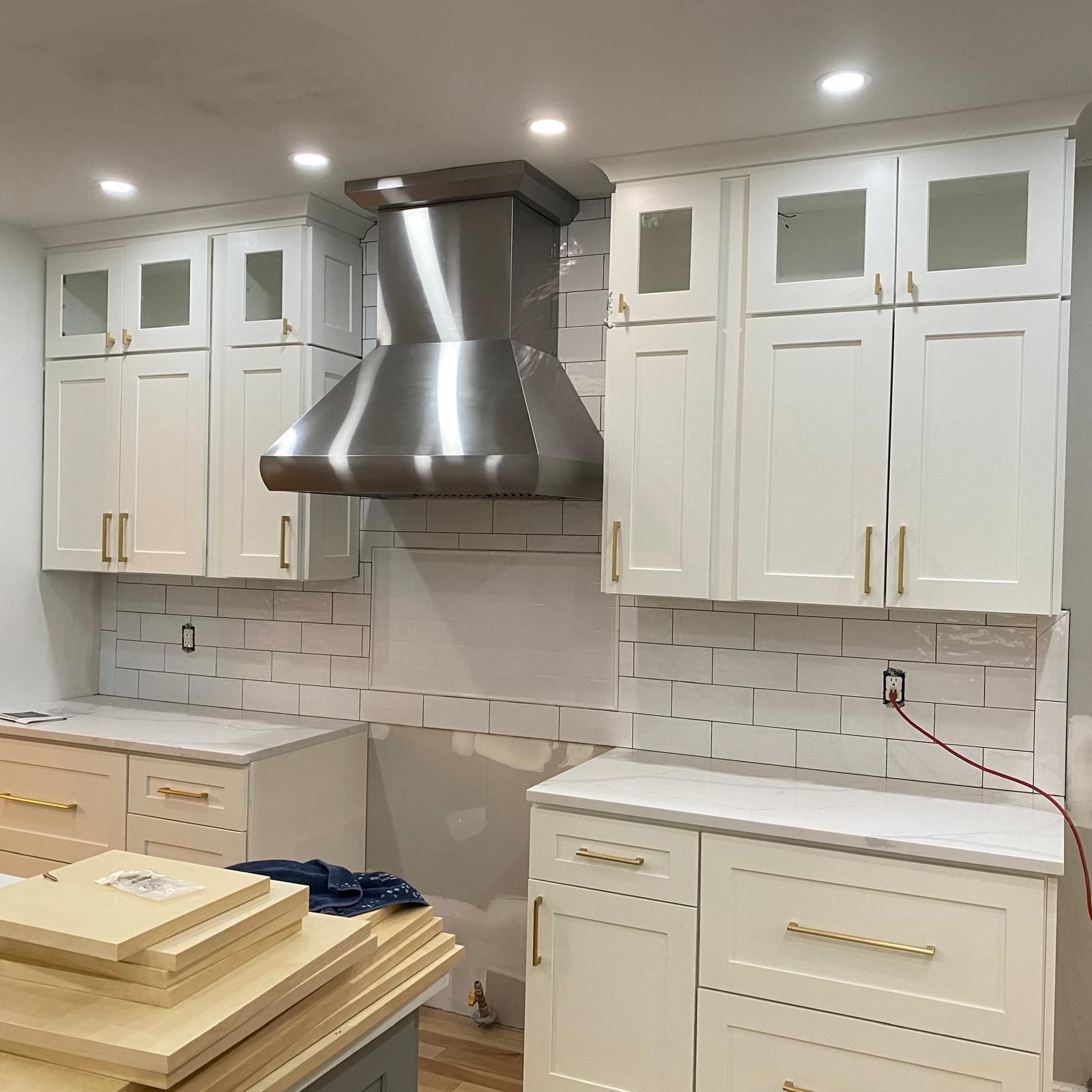 Bright white kitchen with stainless range hood, white cabinets, and countertop materials stacked in the foreground