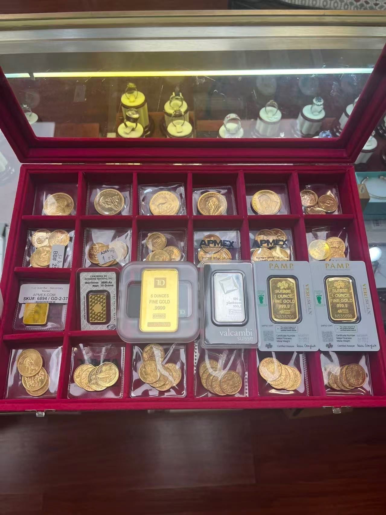 A red-lined jewelry display case filled with gold bars and coins, organized in individual compartments.