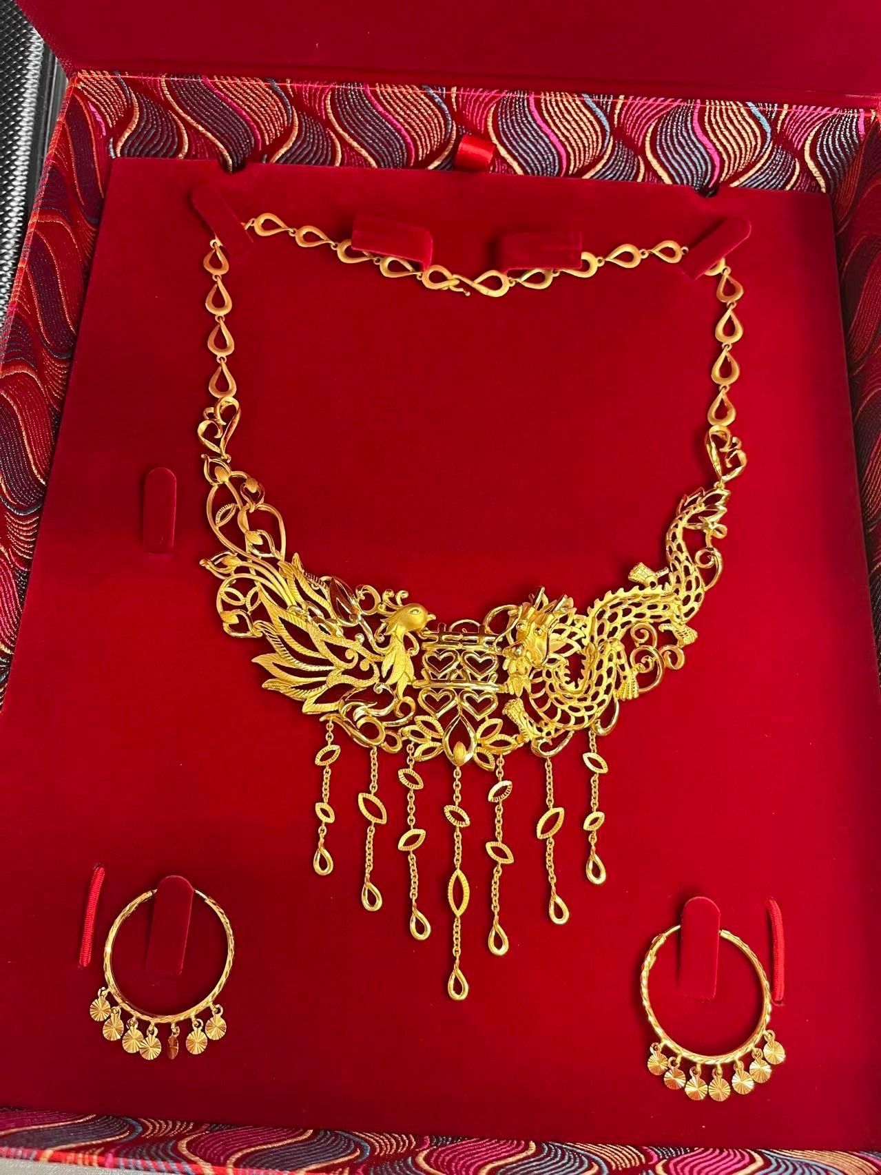 A gold-toned necklace and matching hoop earrings with hanging charms, displayed in a red velvet-lined presentation box.