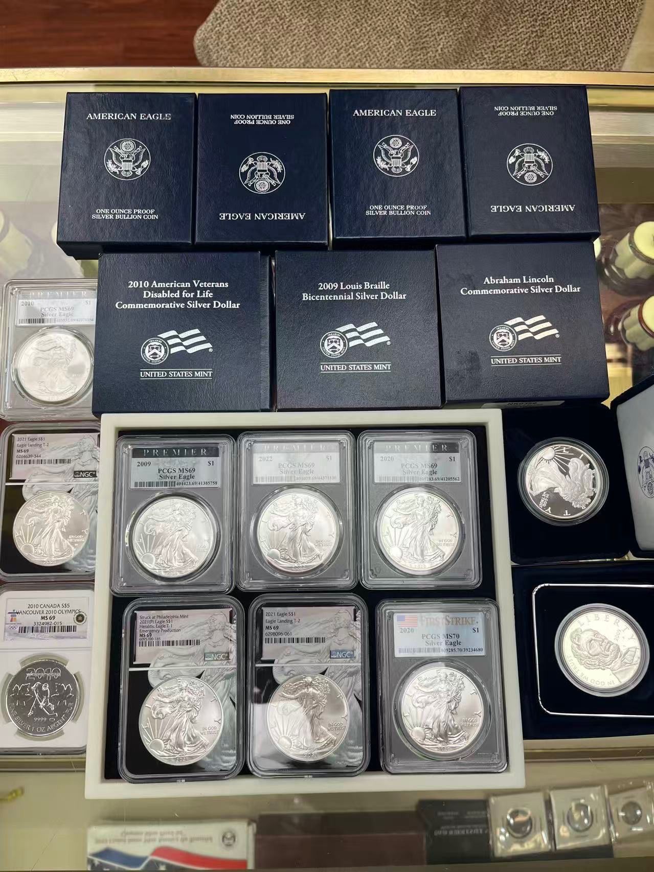 A display of collectible silver coins in protective plastic cases and labeled dark blue display boxes on a table.