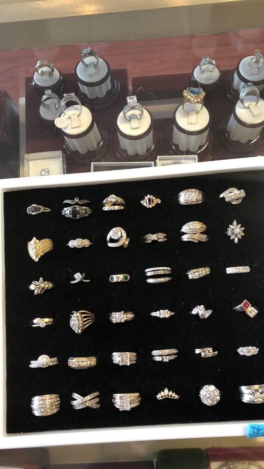 Jewelry display case with many rings on black velvet. Some on stands, others flat. Mostly silver and diamonds.