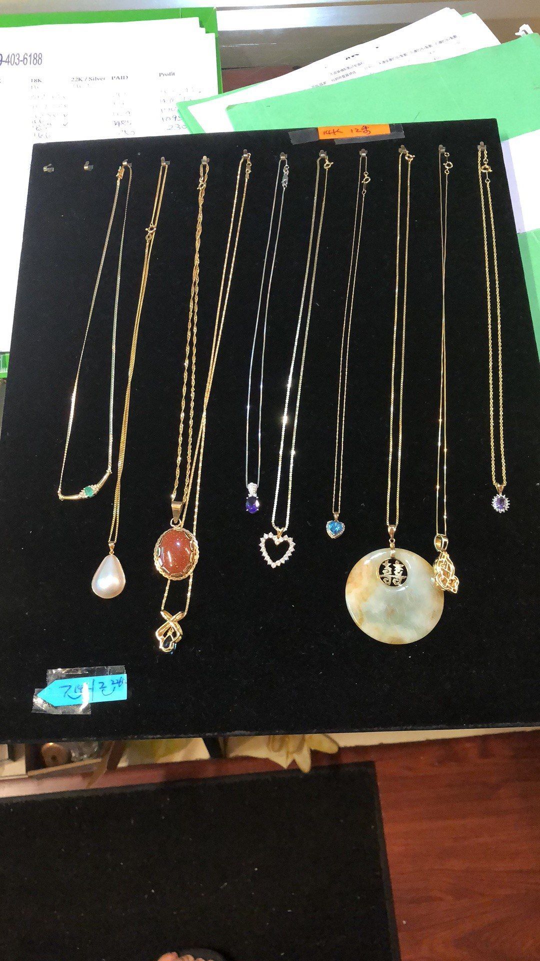 Ten gold necklaces with pendants displayed on a black surface.