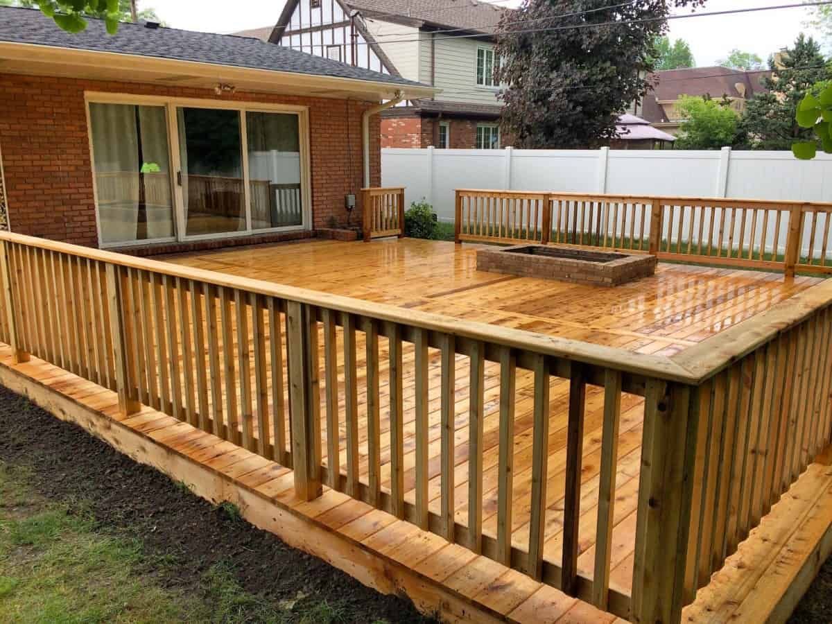 A wooden deck with a fire pit in the backyard of a house.