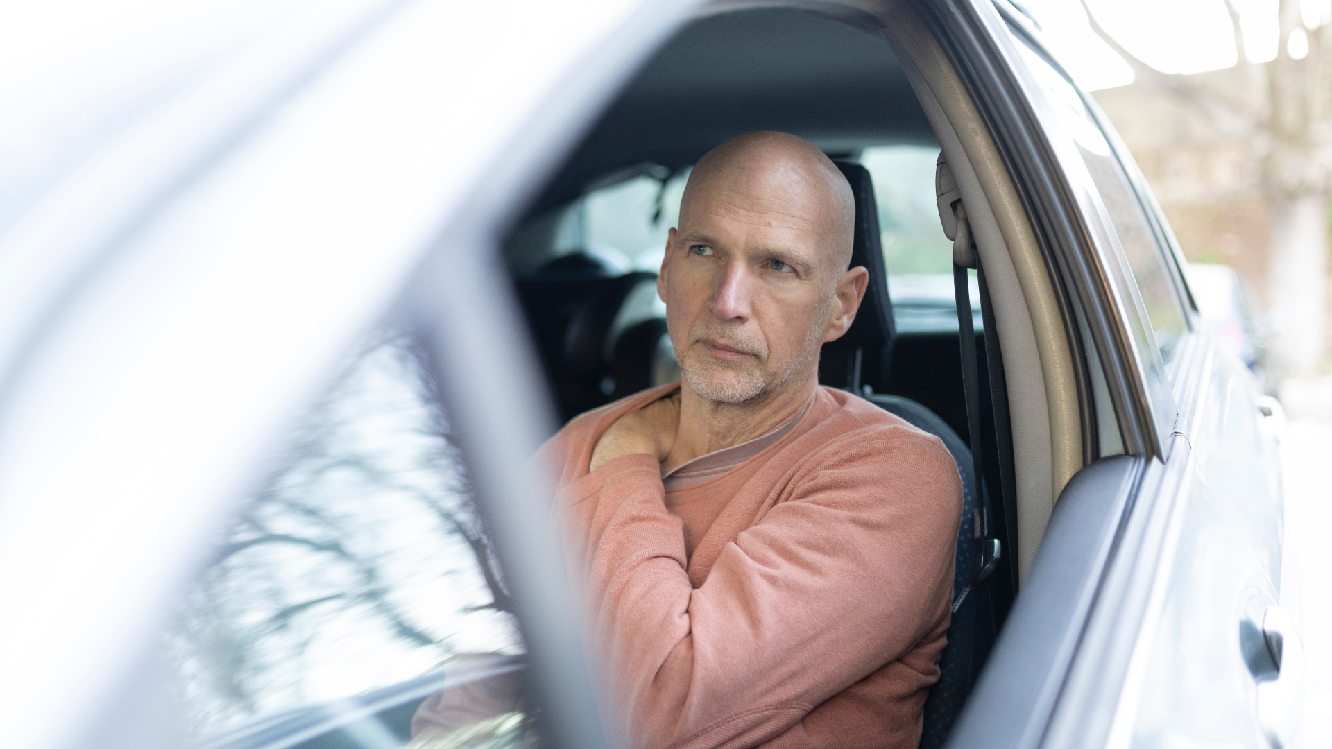 Man sitting in a car rubbing his trapezius, looking worried about minor pain after a car accident.