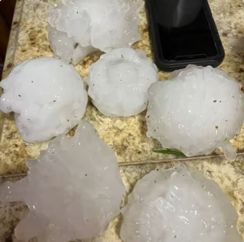 A bunch of hailstones is sitting on a counter next to a cell phone.