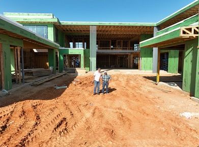 Two men are standing in front of a large building under construction.