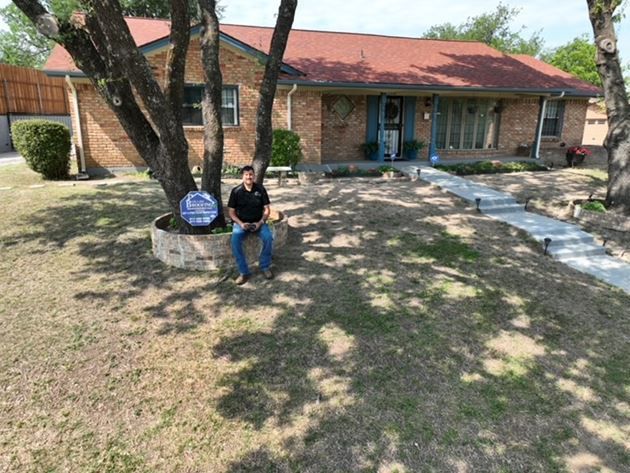 A man is sitting under a tree in front of a house