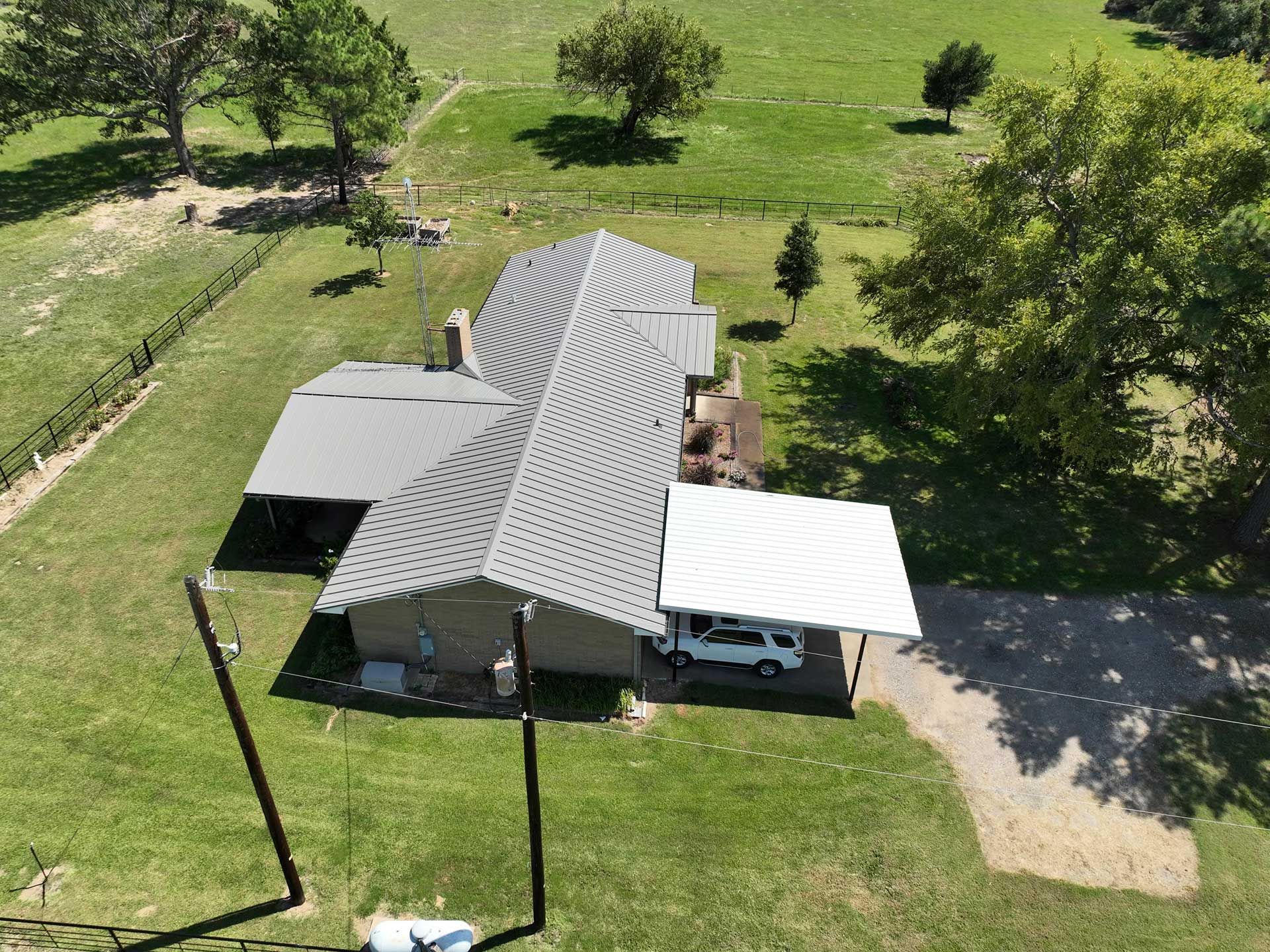 An aerial view of a house with a new roof in the middle of a grassy field