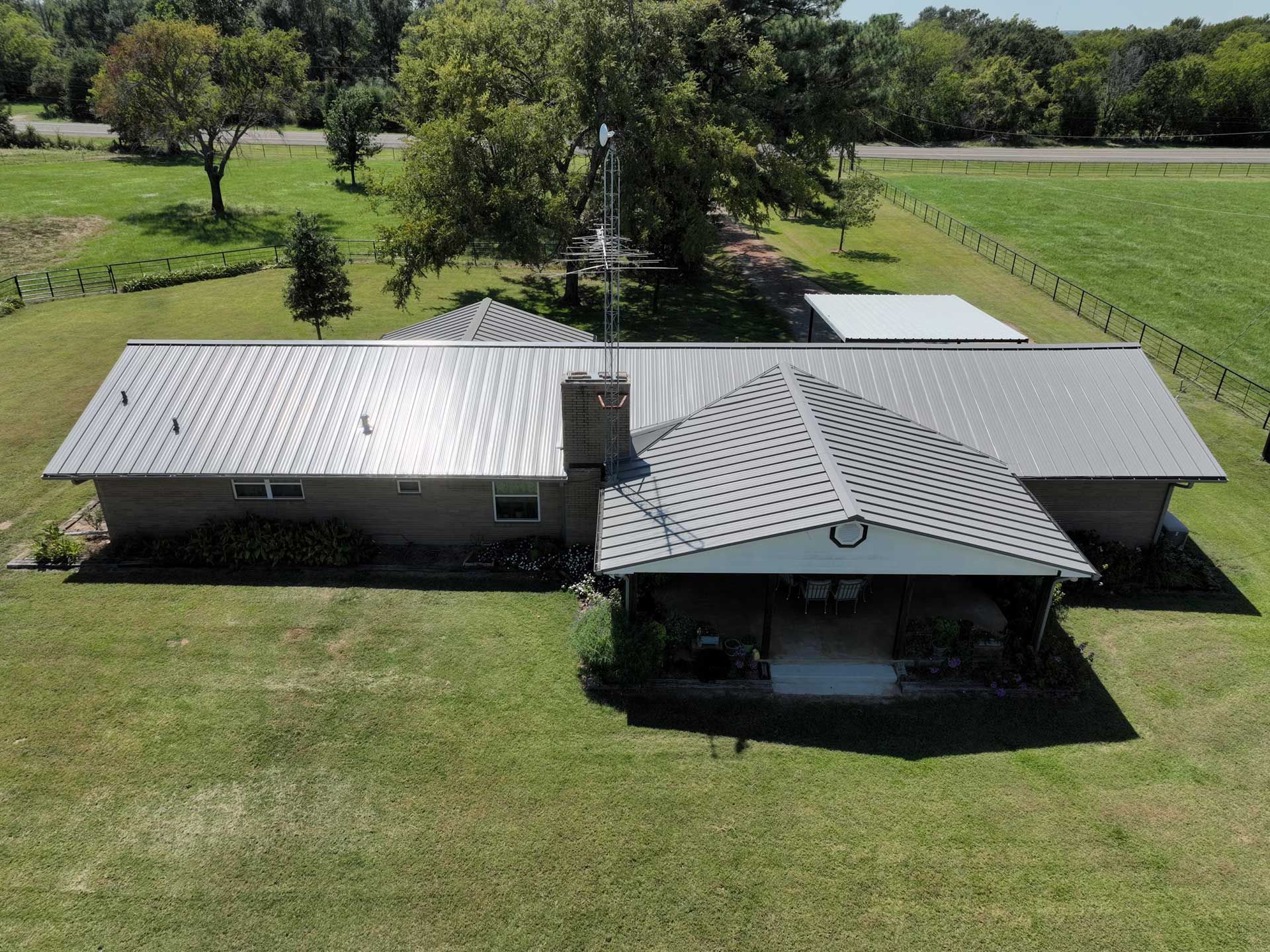 An aerial view of a house with a metal roof in a grassy field