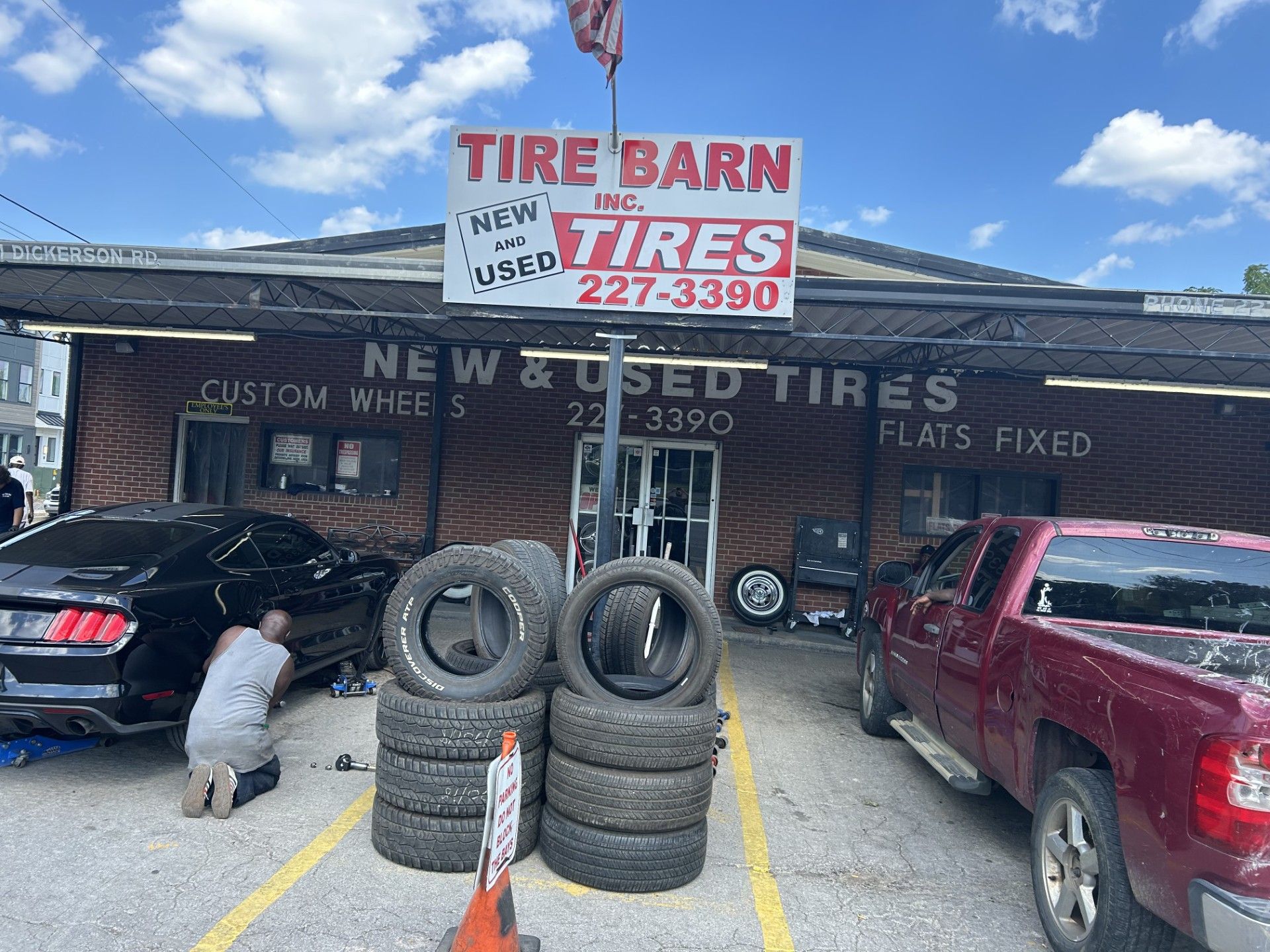 A man is working on a car in front of a tire barn.