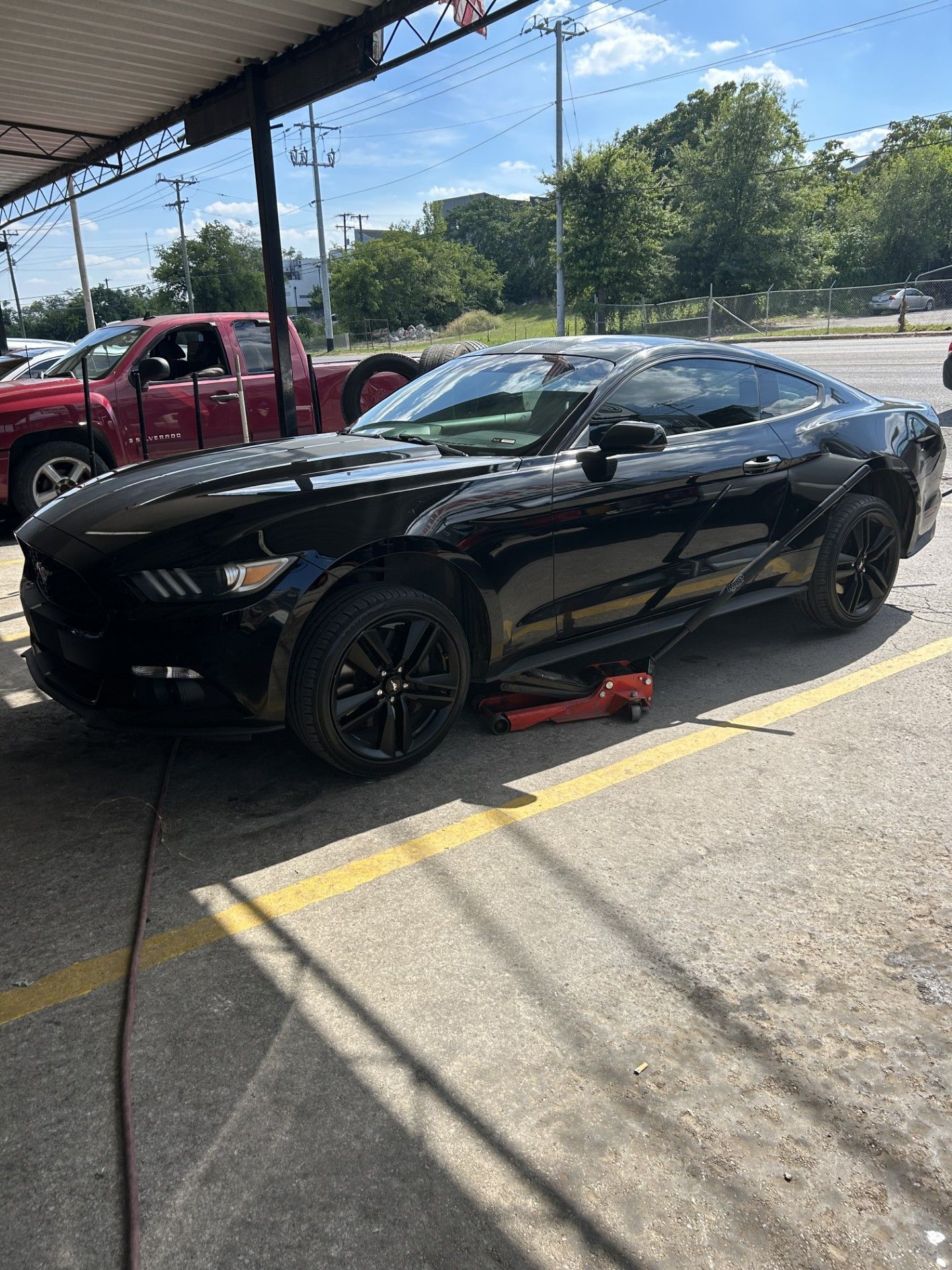 A black mustang is sitting on a jack in a parking lot.