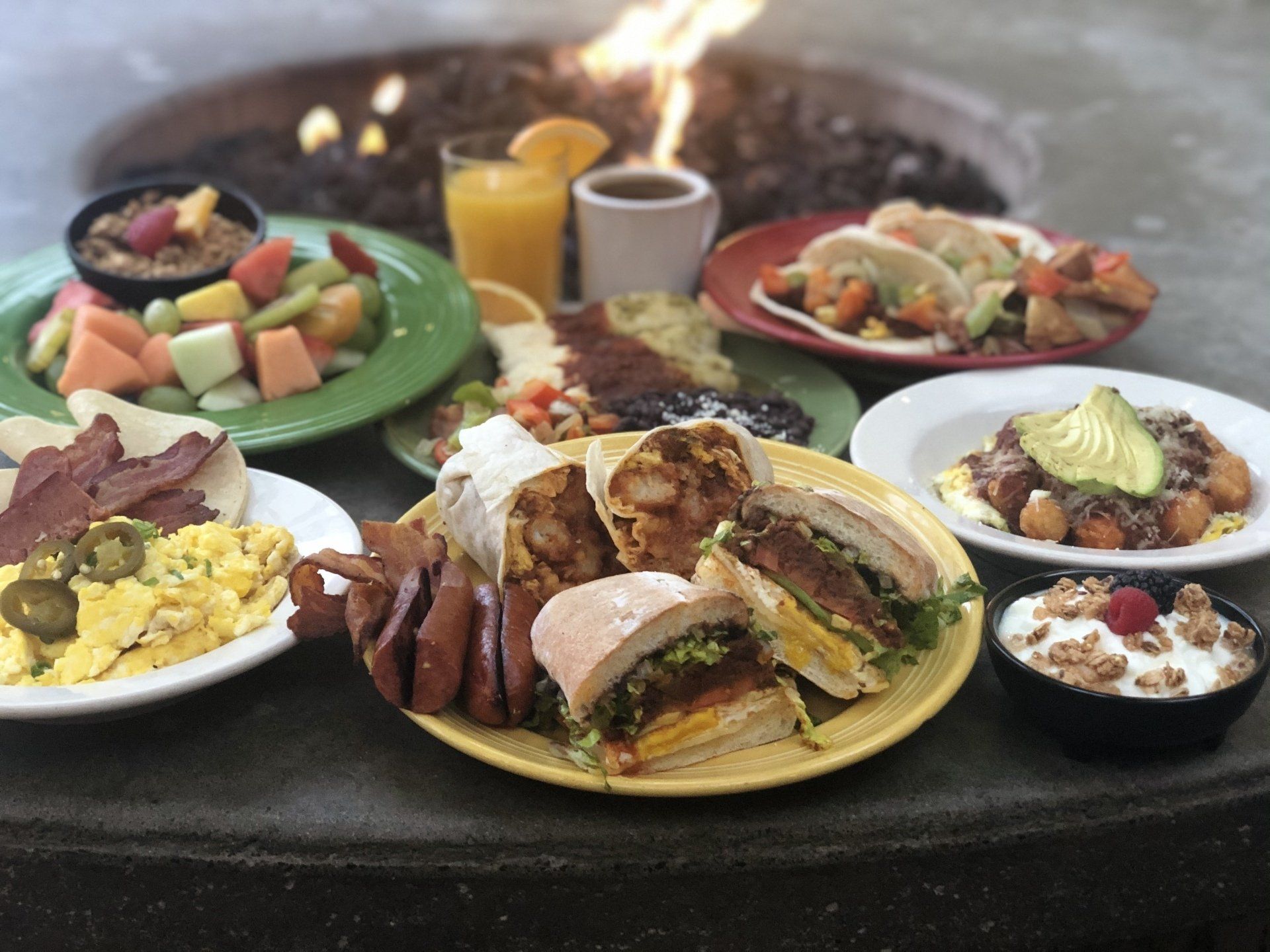 A table topped with plates of food and a fire pit in the background