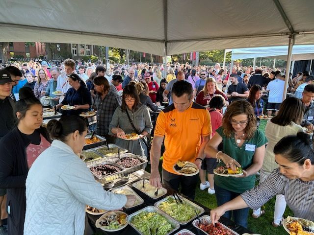 a large group of people are standing around a buffet table eating food