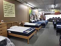 Mattress store with several beds on display. Brown wooden frames, gray carpet, sign on wall.